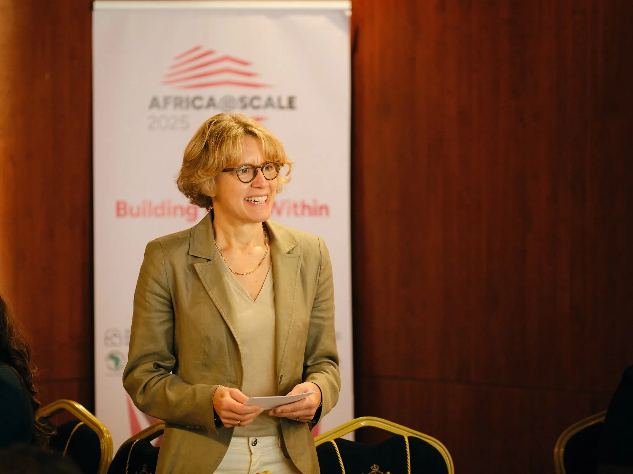 A speaker holds her notes in front of an event banner.